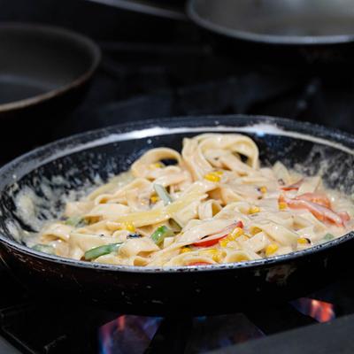 Creamy fettucine pasta with vegetables cooking in a pan.
