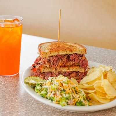 Pastrami Reuben sandwich served with sides and a drink.