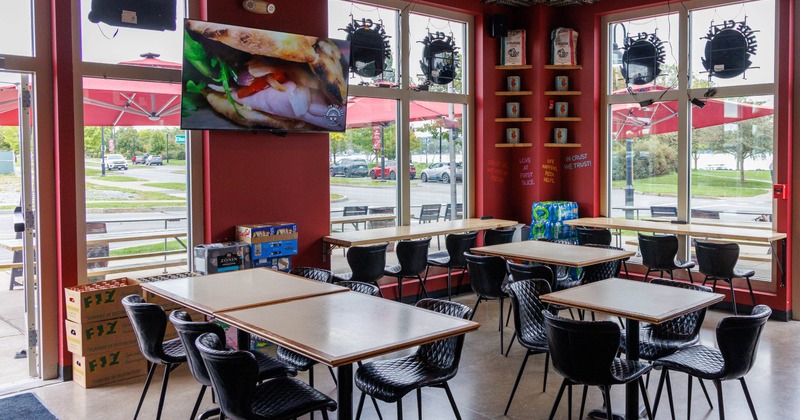Inside, dining area with tables, black chairs, large windows, pizza-themed wall text