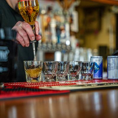 A bartender pouring drink into shot glasses on a bar counter.