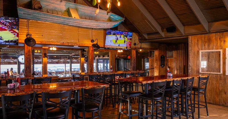 Interior, high long tables and chairs, big TV screens on the wall