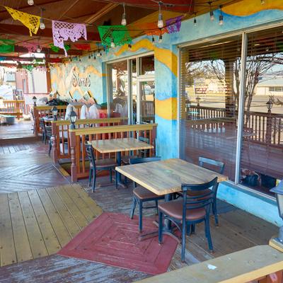Covered patio with wooden tables, string lights, and papel picado decorations.