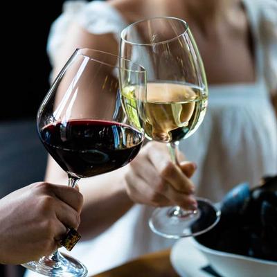 Two people clink glasses of red and white wine over a table with a bowl of mussels.