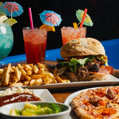 A vibrant spread featuring a burger with fries, a pepperoni pizza, ribs, and colorful  cocktails.