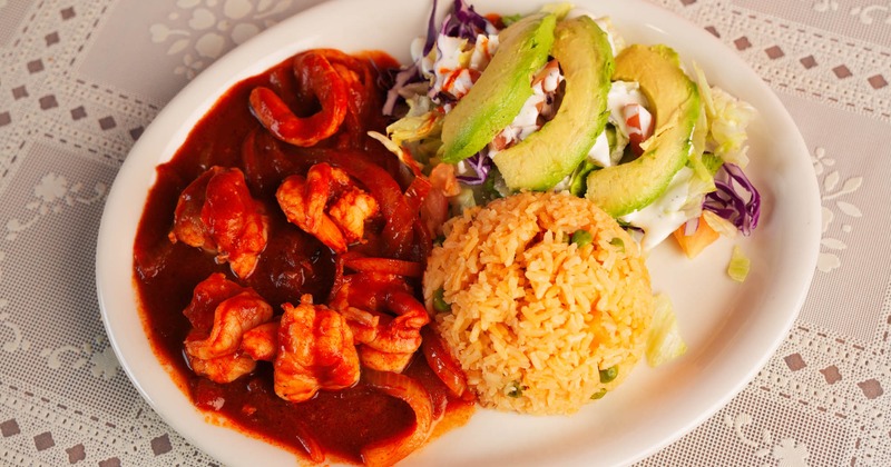 Spicy shrimp in red sauce with rice, avocado slices, and colorful salad
