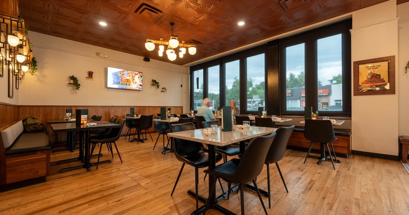 Interior of a modern restaurant with wooden floors, marble tables, and a decorative ceiling