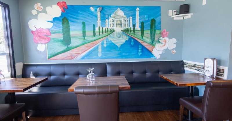 Interior with a mural of the Taj Mahal, with two wooden tables and a black booth