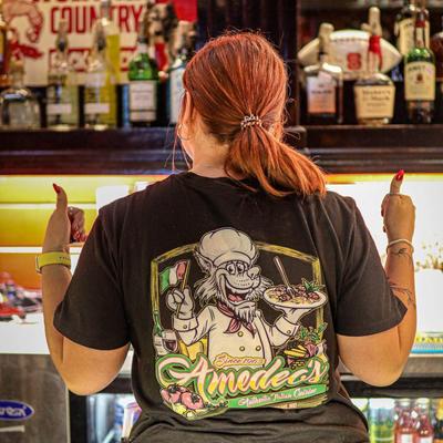 A bar employee wearing Amedeo's shirt gives thumbs up at camera.