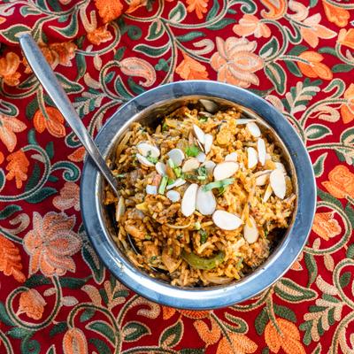 Chicken biryani topped with sliced almonds, served on a floral tablecloth.