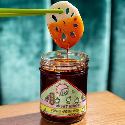 Chopsticks dipping lotos root piece into a jar of vegan pickled chili paste.