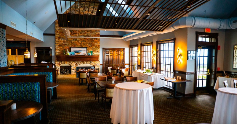 A modern restaurant interior with a stone fireplace, large windows, and elegant decor