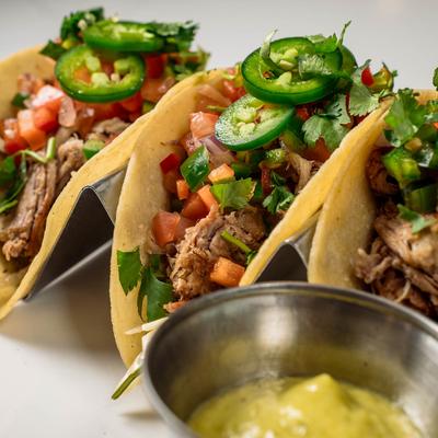 Three hard-shell carnitas tacos topped with fresh salsa, jalapenos, and cilantro.