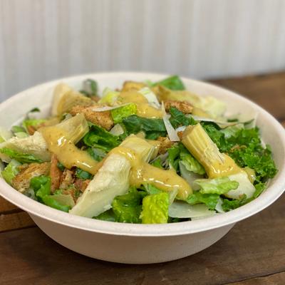 Caesar salad with artichoke hearts and  parmesan shavings, topped with dressing.