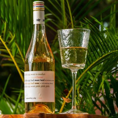 Squealing pig rosé wine, bottle and glass resting in front of palm branches.