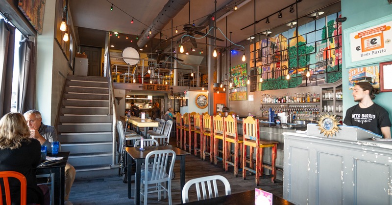 The restaurant's interior, a staircase, tables, chairs, and stools at the bar