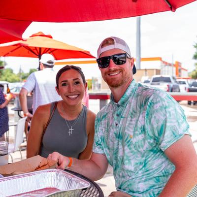 Two people smiling at an outdoor table under red umbrellas.