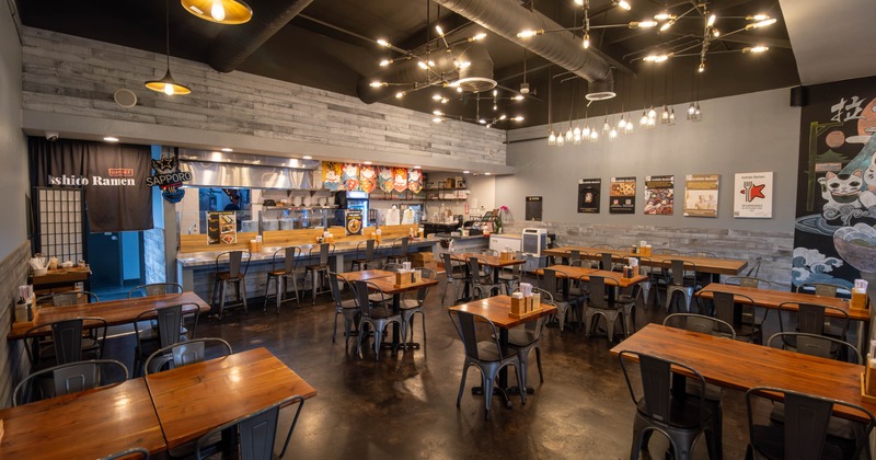 Interior of a modern ramen restaurant with wooden tables, metal chairs, exposed bulbs