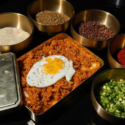 Kimchi fried rice surrounded by small brass bowls filled with spices and chopped scallions.