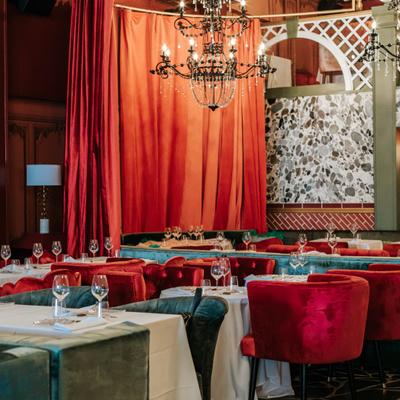 Interior dining room with red curtains dim lighting and set tables.