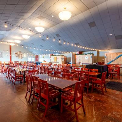Large event hall with wooden tables, red chairs, and string lights.
