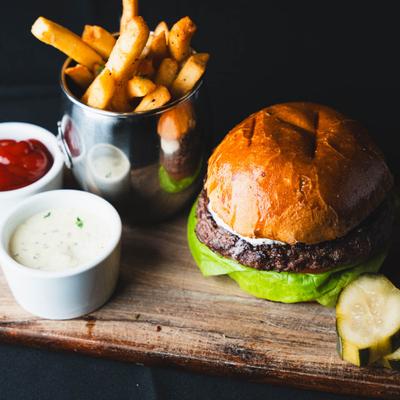 Beef burger with lettuce accompanied by fries, dipping sauces, and pickles.