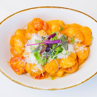 Gnocchi in creamy orange sauce topped with grated cheese and fresh microgreens.