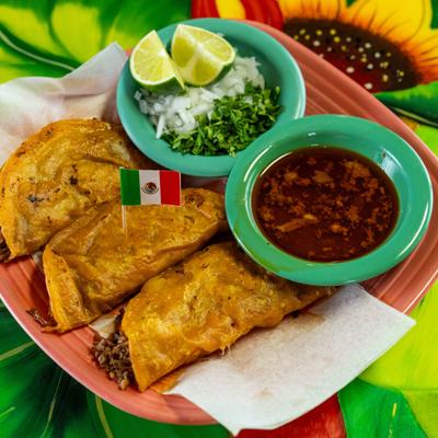 Birria tacos with consomme, onions, cilantro, and lime.
