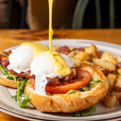 Golden hollandaise drips over BLT Benedict with breakfast potatoes.