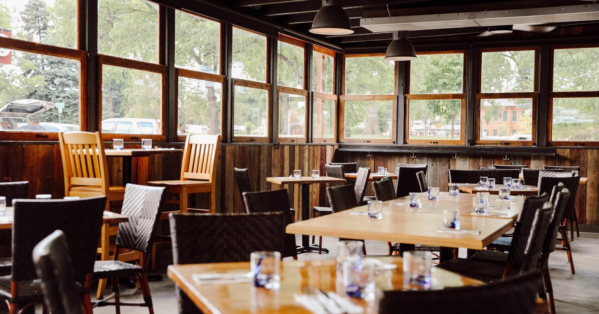 Bright dining area with wooden tables, wicker chairs, and large windows