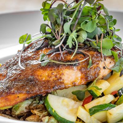 Grilled salmon topped with microgreens, served over sauteed vegetables.
