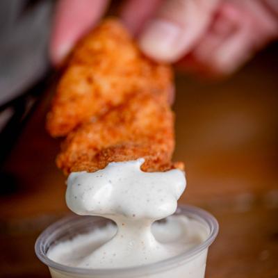 A hand dipping fried chicken.