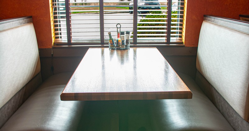 Restaurant booth - a wooden table between two light gray padded benches, against a window