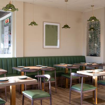 Interior with a green leather banquette bench, set tables, and pendant lights.