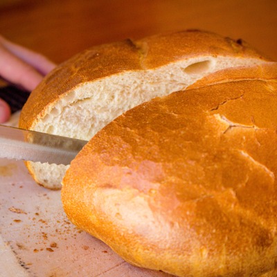 A serrated knife slices through a round loaf of bread.