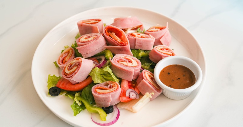 Antipasto salad featuring rolled Italian meats, fresh veggies and a cup of dressing