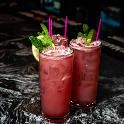 Berry-infused tall cocktails served over ice, garnished with fresh mint and lime wedges.
