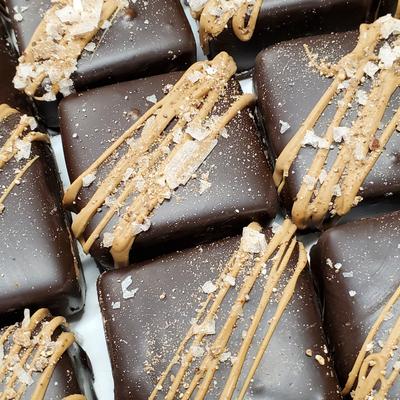 Close-up of chocolate-covered squares adorned with caramel drizzle and sprinkled sea salt.