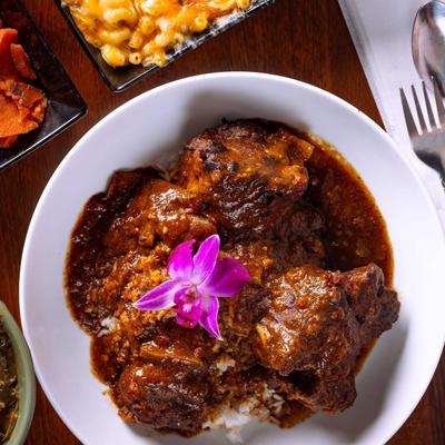 Braised oxtail served over rice, alongside various side dishes, overhead view.