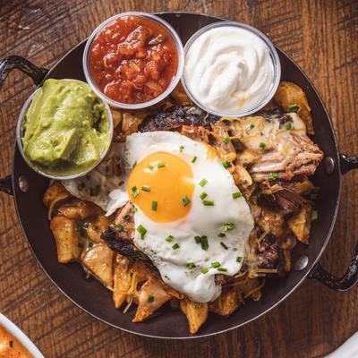 Breakfast nachos with brisket, fried egg, cheese, home fries, guacamole, and salsa