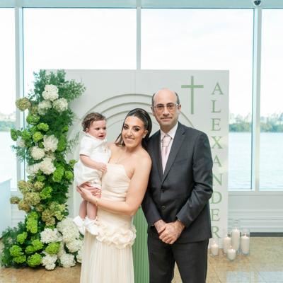 Couple with a child standing beside a white floral ceremony arch.