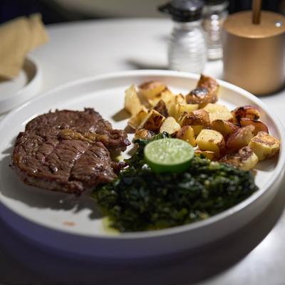 Steak served with roasted potatoes and sauteed greens.