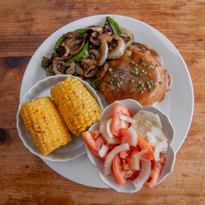 Hamburger steak with corn on the cob and a fresh tomato-onion salad.