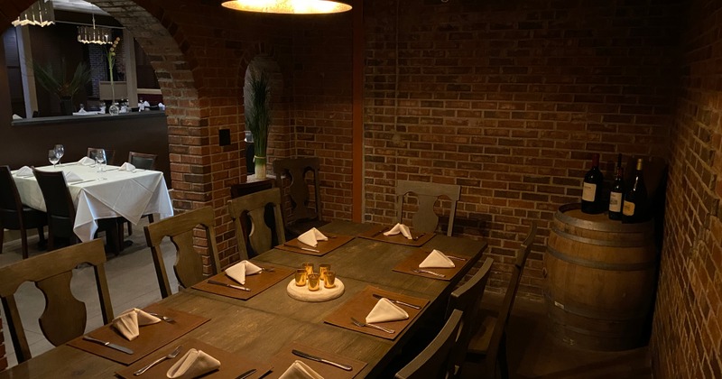 Main dining room with brick walls, white clothed tables with wine glasses and silverware settings.