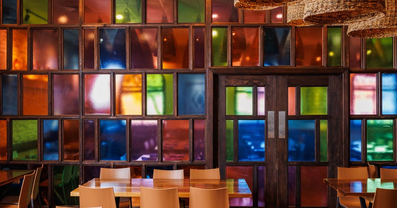 Interior, tables and chairs in front of colorful glass wall