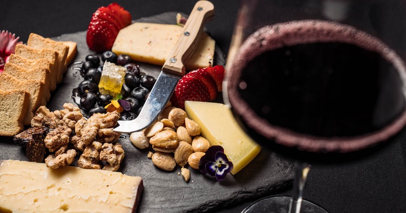 Artisan Cheese Board served with berries, almonds, and a glass of red wine