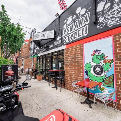 Brick storefront of Puglia Pizza with outdoor tables and cartoon character artwork.
