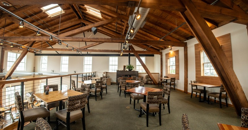 Interior of a rustic restaurant with wooden beams, tables, and plush chairs