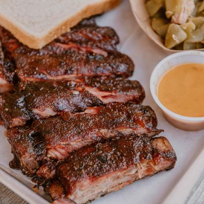 BBQ ribs served with sides of green beans, dipping sauces, and sliced white bread.