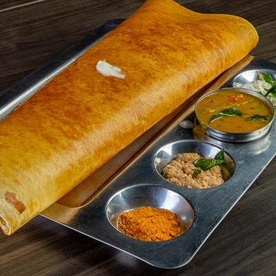 Folded dosa with chutneys on metal platter.
