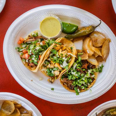 Taco platter featuring a variety of meats, served with a side of green salsa, grilled onions, and a jalapeno.
